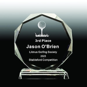 May include: A clear, faceted crystal trophy with a golf ball graphic and the text "3rd Place Jason O'Brien Litmus Golfing Society 2025 Stableford Competition". The trophy sits on a rectangular base.