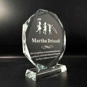Puede incluir: Un premio de cristal transparente con un dise&ntilde;o facetado. El premio presenta una imagen grabada de ni&ntilde;os y el texto "Martha Driscoll" y "En reconocimiento a la dedicaci&oacute;n, orientaci&oacute;n y liderazgo sobresalientes como tesorero de PA para Park Children's Day School."