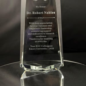 May include: A clear, tapered glass award trophy featuring an etched inscription that reads: We Honor Dr. Robert Nables. With deep appreciation for your visionary and empathetic leadership, unwavering support and dedication to research excellence.