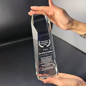 May include: A clear, faceted glass award trophy featuring an etched laurel wreath design and the text: Excellence in Leadership Award, Dr. Robert Nables, We Honor, With deep appreciation for your visionary and empathetic leadership, 2026.