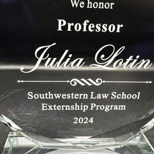 Puede incluir: Un premio de cristal transparente con el texto "We honor Professor Julia Lotin" en letras blancas. El premio tambi&eacute;n incluye "Southwestern Law School Externship Program 2024". La base del premio tiene un dise&ntilde;o geom&eacute;trico.