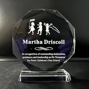 Puede incluir: Un premio de cristal claro y facetado con una base rectangular. El premio presenta el nombre "Martha Driscoll" y una inscripci&oacute;n que reconoce la dedicaci&oacute;n excepcional. Un gr&aacute;fico de ni&ntilde;os est&aacute; grabado en la parte superior.