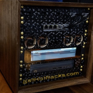 May include: A wooden server rack enclosure featuring a black geometric patterned front panel, gold-colored screws, four circular cooling fans, a horizontal display screen, an HP device, and the text getHotRacks.com printed in gold at the bottom.