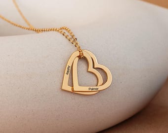 Op de afbeelding: Gouden ketting met twee in elkaar grijpende hartvormige hangers. De harten zijn gegraveerd met de namen "Ashley" en "Palmer".