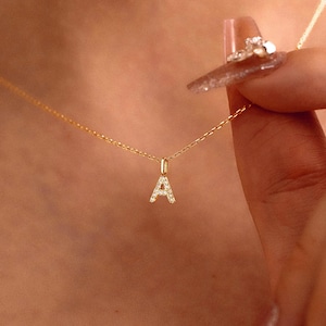 May include: A fine gold necklace with a pendant shaped like the letter "A", set with tiny, glittering gemstones. The chain is slender and graceful, with the pendant centrally placed. This necklace is a piece of jewellery.