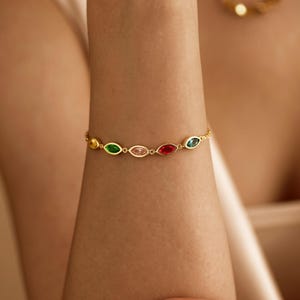 Könnte beinhalten: Ein goldfarbenes Kettenarmband mit einer Reihe von marquise-geschliffenen Edelsteinen in verschiedenen Farben, darunter Gelb, Grün, Hellrosa, Rot und Blau. Die Steine sind in einzelnen goldfarbenen Metallfassungen aneinandergereiht.