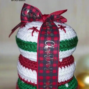 May include: A stack of three crocheted Christmas ornaments in red, white, and green, tied with a red and black plaid ribbon with the text "Merry Christmas" printed on it.