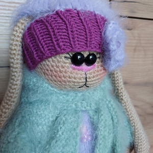 May include: A crocheted bunny wearing a purple hat with a flower and a light green fuzzy coat.