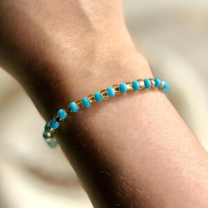 May include: A beaded bracelet with alternating turquoise and gold beads. The bracelet is made of small, round beads strung together. The bracelet is worn on a wrist. The beads are approximately 0.5 cm in diameter.