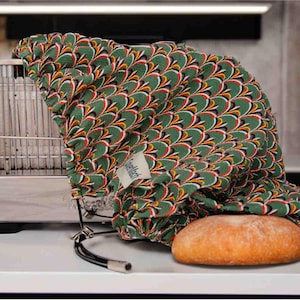 May include: A green and yellow patterned fabric bag with a drawstring closure, holding a loaf of bread. The bag is sitting on a white countertop next to a silver toaster.