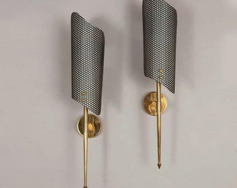 May include: Pair of mid-century modern sconces. Each sconce features a perforated black shade with white dots, a brass-colored stem, and a circular wall mount. The sconces are mounted on a light gray wall.