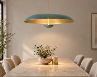 Puede incluir: Una lámpara colgante grande y ancha en forma de platillo, con un exterior en color verde azulado mate y un interior dorado reflectante. La pieza cuelga de una varilla de latón y tiene un pequeño difusor circular a juego bajo la pantalla.