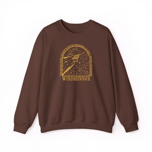 Puede incluir: Una sudadera marr&oacute;n con un dise&ntilde;o gr&aacute;fico dorado. El dise&ntilde;o presenta una imagen estilizada de una persona con una espada, estrellas y el texto "WINDRUNNER". Tambi&eacute;n incluye el texto "LIFE BEFORE DEATH, STRENGTH BEFORE WEAKNESS, JOURNEY BEFORE DESTINATION".