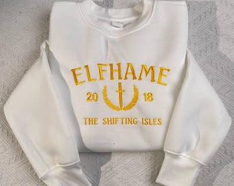 May include: White crewneck sweatshirt with gold embroidery that reads "Elfhame 20 18 The Shifting Isles".