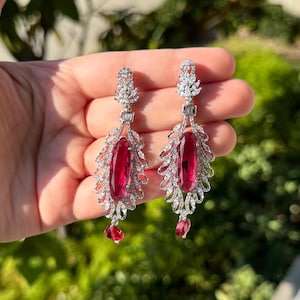 May include: A pair of silver dangle earrings with a red gemstone and clear crystal accents.