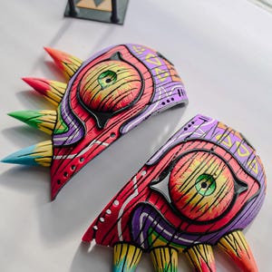 Op de afbeelding: Een 3D-geprint Majora's Mask uit het videospel The Legend of Zelda: Majora's Mask. Het masker is geschilderd in verschillende kleuren, waaronder rood, geel, groen, blauw en paars. Het masker is in twee delen gesplitst en de ogen zijn zichtbaar.