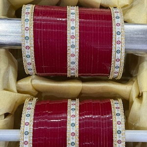 Può includere: Un set di due braccialetti rossi con accenti decorativi bianchi e dorati. I braccialetti sono adornati con piccoli strass trasparenti.