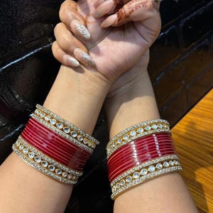 Può includere: Un paio di braccialetti rossi e dorati con pietre bianche. I braccialetti sono decorati con una fila di pietre bianche attorno al bordo.