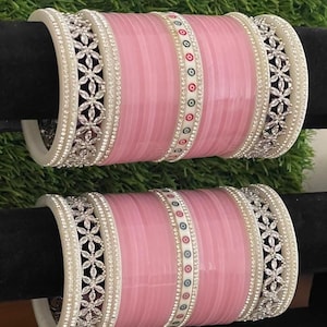 Può includere: Due set di braccialetti rosa con accenti bianchi e argentati. I braccialetti sono decorati con piccole pietre bianche e un motivo floreale.