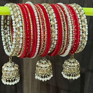 May include: A set of red and gold bangles with white pearl accents and dangling gold charms. The bangles are decorated with small rhinestones and beads.