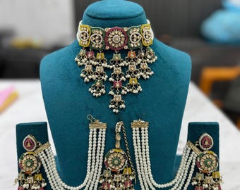 May include: An ornate jewelry set featuring a choker necklace, earrings, and a headpiece. The set includes a white choker with colorful accents, dangling pendants, and pearl strands. The earrings and headpiece mirror the necklace's design, with colorful gems and pearls.