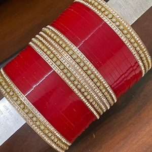 Op de afbeelding: Een stapel rode armbanden met gouden en parelaccenten. De armbanden zijn versierd met kleine, ronde parels en heldere, sprankelende stenen. Het ontwerp heeft een combinatie van rode, gouden, witte en heldere elementen, wat een luxueuze uitstraling creëert.