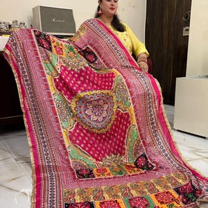 May include: A pink and green patterned shawl with gold trim and sequins. The shawl features a large circular design in the centre and a patchwork design at the bottom.