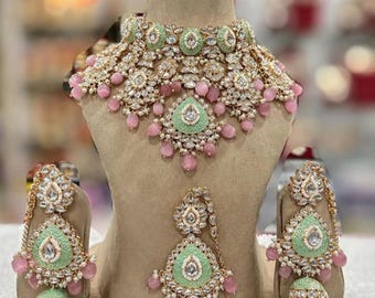 May include: A traditional Indian bridal jewelry set featuring a green and pink necklace, earrings, and a nose ring. The set is adorned with pearls, stones, and gold accents.