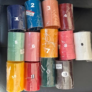 May include: Thirteen colorful round bobbins, numbered 1 through 13, are arranged in three rows. The bobbins are made of a translucent material and have a slightly textured surface. The bobbins are all different colors, including blue, green, orange, red, pink, white, yellow, and brown.