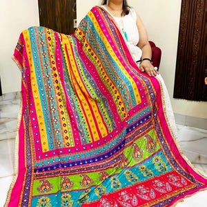 May include: A colourful patterned shawl with mirrored embellishments and a fringe border. The shawl is made of a soft, flowing fabric and features a variety of colours, including pink, yellow, blue, green, and red.