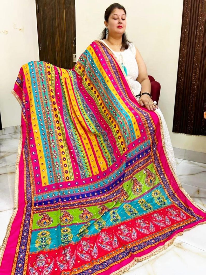 May include: A colourful patterned shawl with mirrored embellishments and a fringe border. The shawl is made of a soft, flowing fabric and features a variety of colours, including pink, yellow, blue, green, and red.