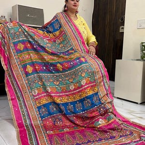 May include: A colourful, multi-patterned shawl with a pink border and gold accents. The shawl is made of a soft, flowing fabric and features intricate embroidery and mirror work.