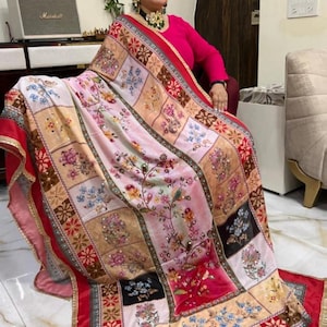 May include: A colourful patterned shawl with a red border and floral embroidery. The shawl is made of a soft, flowing fabric and features a patchwork design with various colours and patterns.