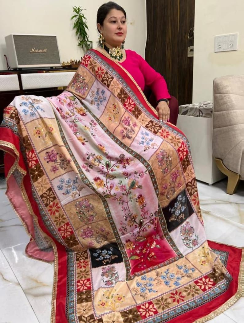 May include: A colourful patterned shawl with a red border and floral embroidery. The shawl is made of a soft, flowing fabric and features a patchwork design with various colours and patterns.