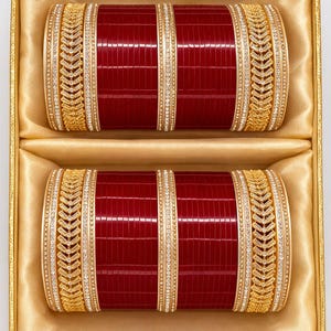 Può includere: Due braccialetti rossi e dorati con dettagli intricati, presentati in una scatola foderata in raso dorato. I braccialetti presentano una superficie rossa strutturata, accentuata da oro e abbellimenti scintillanti. Un bellissimo set per occasioni speciali.