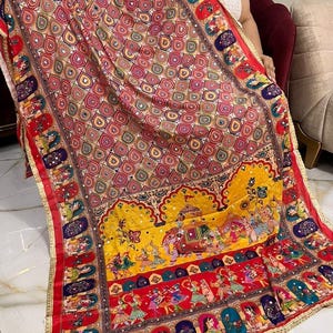 May include: A colourful silk shawl with a paisley pattern and intricate embroidery. The shawl features a border with a repeating design of dancing figures and a yellow elephant.