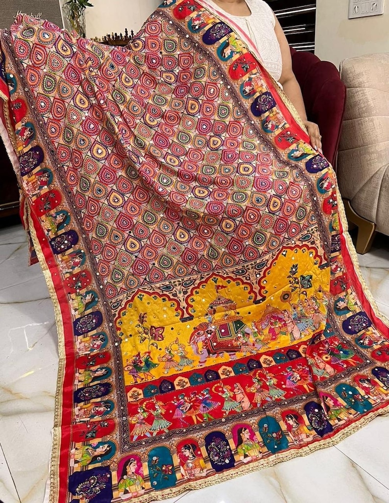 May include: A colourful silk shawl with a paisley pattern and intricate embroidery. The shawl features a border with a repeating design of dancing figures and a yellow elephant.