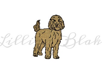 May include: A tan-colored embroidered dog, likely a Goldendoodle, stands facing forward on a white background. The dog has a fluffy coat, a curly tail, and a friendly expression. The name "Lilli Blake" is written in cursive in the background.