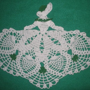 May include: White crocheted doily with a green shamrock design. The doily is shaped like a heart and has a scalloped edge.