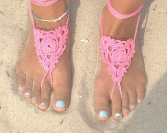 May include: Pink crocheted foot jewelry with a floral design. The jewelry is worn on both feet and has a light blue nail polish on the toes.