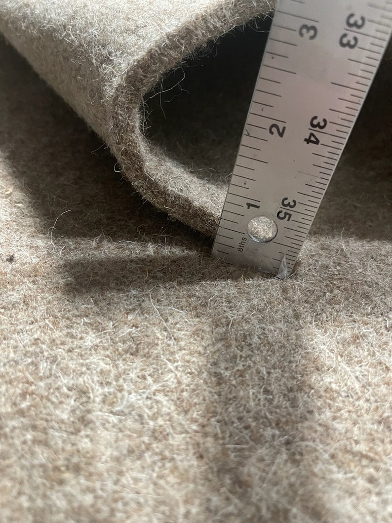 K&ouml;nnte beinhalten: Nahaufnahme eines beigefarbenen Filzstoffs mit einem Lineal, das 84 cm misst. Der Stoff ist weich und texturiert, mit einem leichten Glanz.
