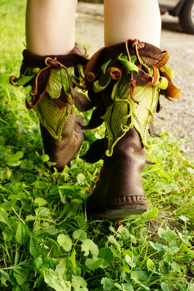 May include: A pair of brown leather boots with green and brown leaf-shaped embellishments. The boots are worn and have a distressed look.