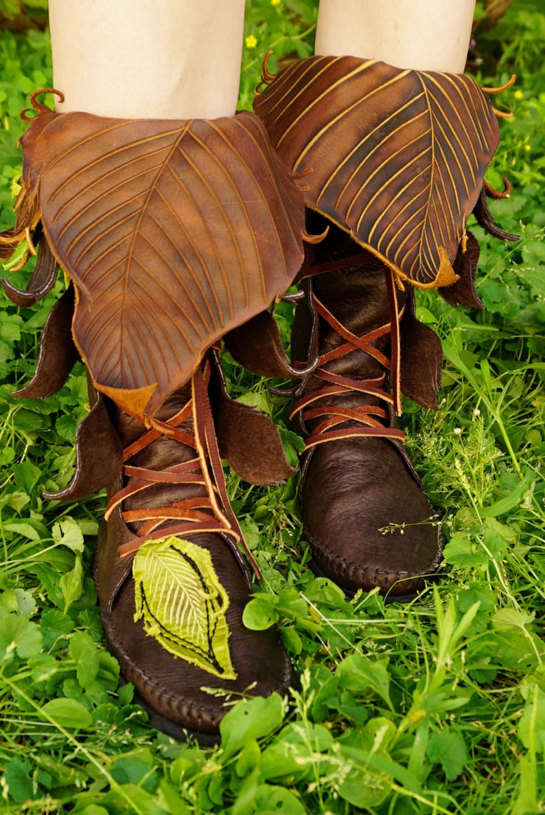 May include: Brown leather boots with leaf-shaped tops and green leaf embroidery. The boots are laced up the front and have a pointed toe.