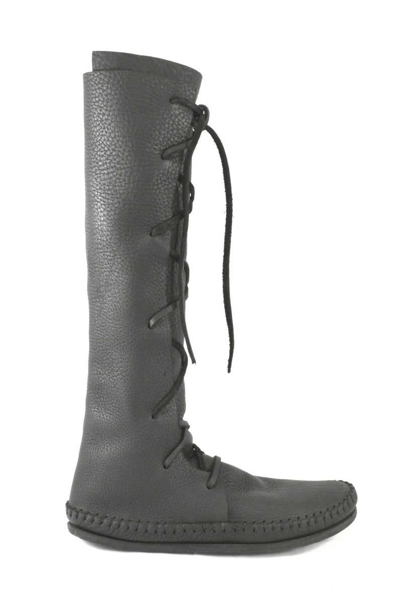 K&ouml;nnte beinhalten: Schwarze, kniehohe Lederstiefel mit Schn&uuml;rung an der Seite und einer Mokassin-Sohle.