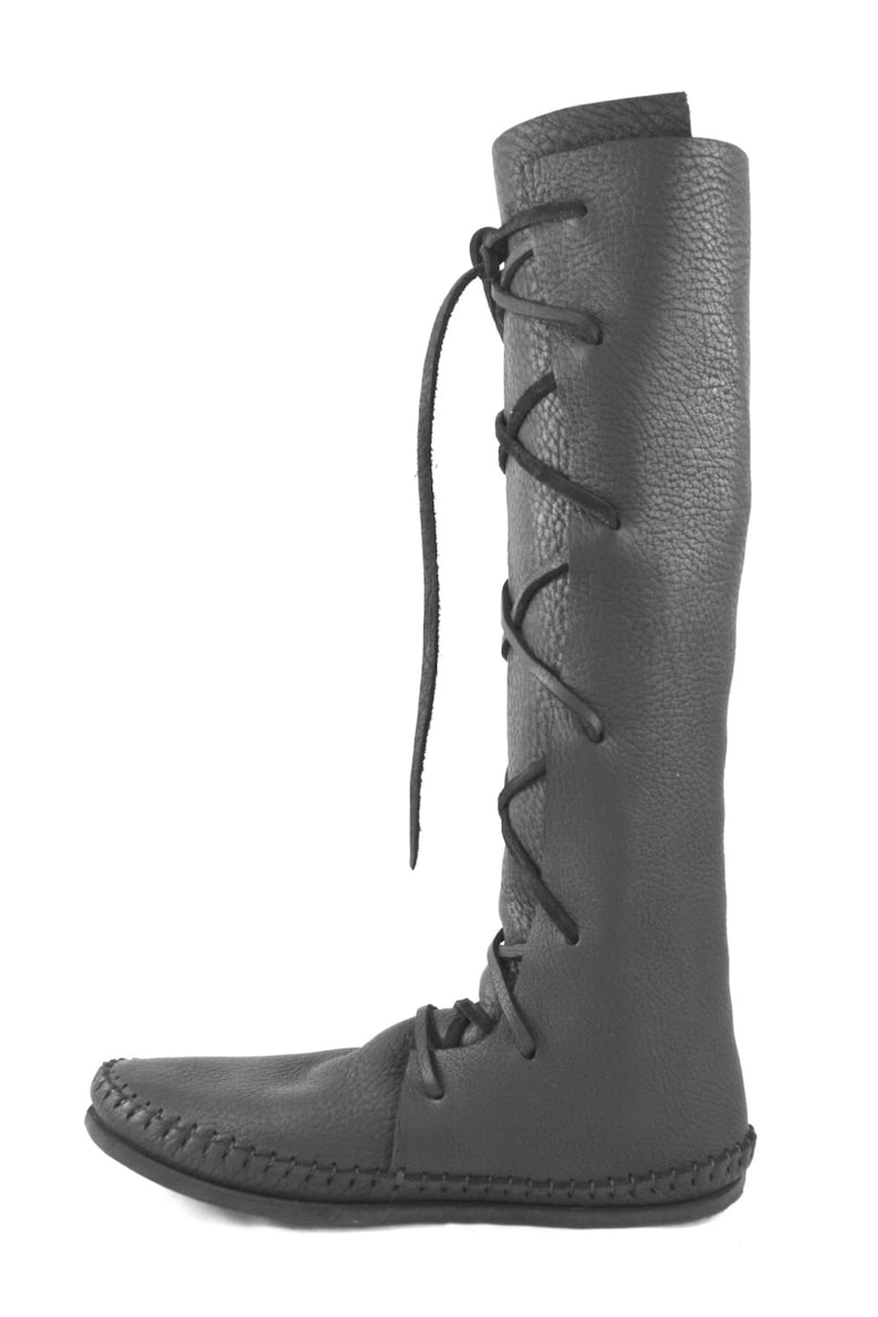 K&ouml;nnte beinhalten: Schwarze, kniehohe Lederstiefel mit Schn&uuml;rung an der Seite. Die Stiefel haben eine Mokassin-Spitze.