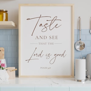May include: A framed print with the text "Taste and See That the Lord is Good" in brown script. The print is in a light wood frame and is displayed in a kitchen setting. Psalm 34:8 is printed below the text.
