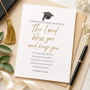 May include: A graduation card with the text "CONGRATULATIONS GRADUATE" and "The Lord bless you and keep you" in gold script. The card includes a graduation cap illustration and a Bible verse. A gold tassel and pen are also visible.