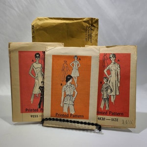 Op de afbeelding: Drie vintage naaipatronen voor jurken en broeken. De patronen zijn gedrukt op papier en hebben een rode achtergrond met zwarte illustraties. De patronen zijn voor maat 14 1/2. De patronen zijn getiteld "Gedrukt patroon" en hebben de nummers 9255 en 4820.