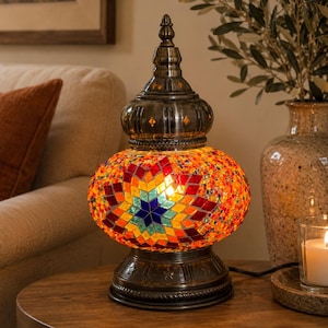 May include: A table lamp featuring a rounded glass shade covered in a colorful mosaic of red, orange, yellow, and blue tiles arranged in a star pattern. The lamp has a dark metallic base and a matching pointed top finial with an antique finish.