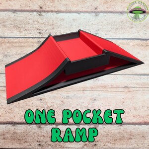 May include: A red and black ramp with the text "ONE POCKET RAMP" in green. The ramp has a curved design and is made of a solid material. The Flying Saucer Printing logo is in the upper right corner.